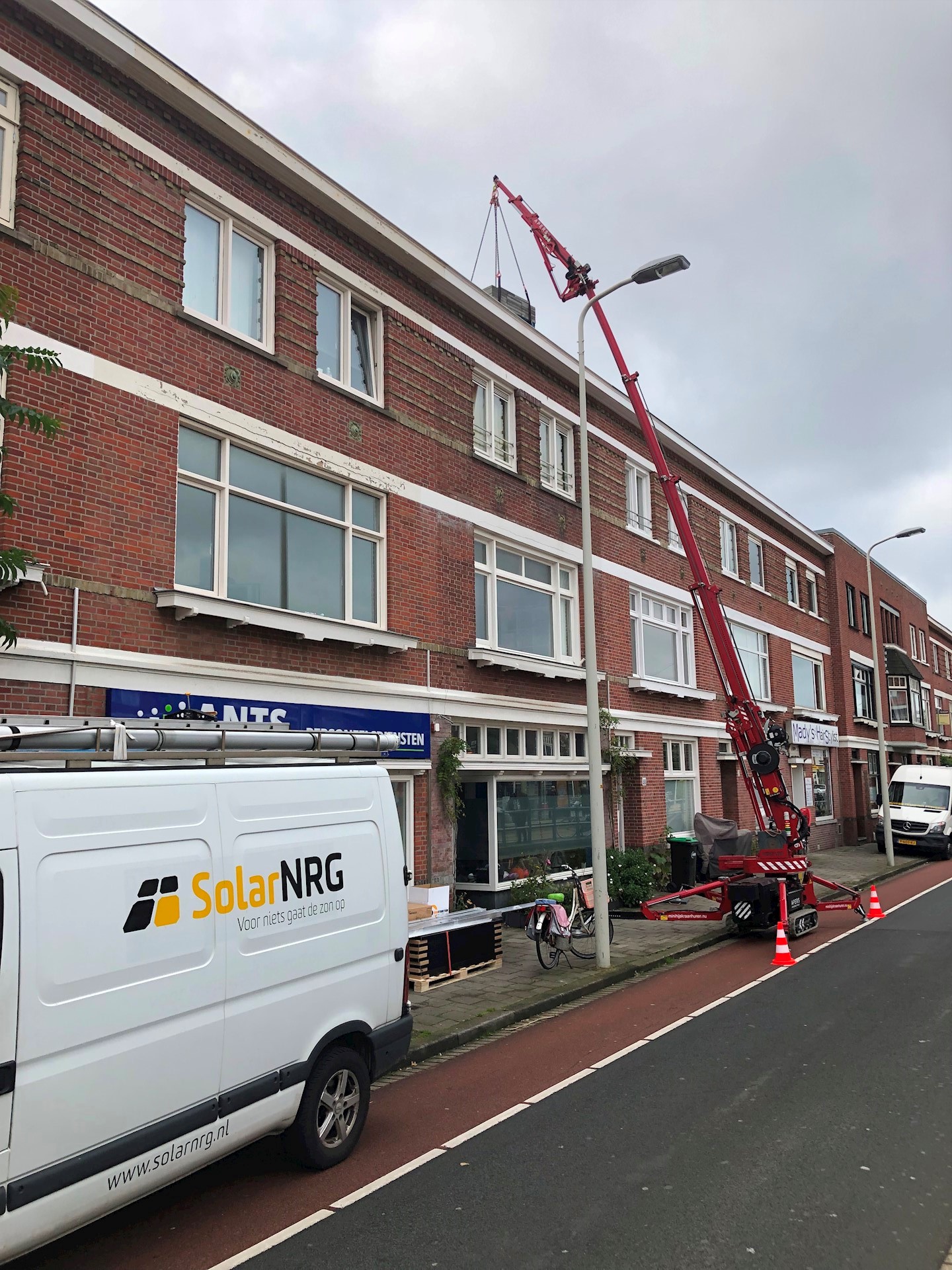 Zonnepanelen hijsen met minihijskraan in drukke straat